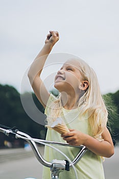 portrait of smiling child with ice cream and bicycle gesturing