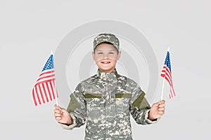 portrait of smiling child in military uniform with american flagpoles in hands