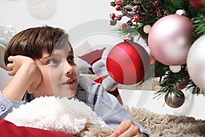 Portrait of smiling child near the christmas tree decorated with balls, comfortable in living room