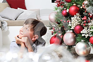 Portrait of smiling child near the christmas tree decorated with balls, comfortable in living room