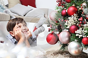 Portrait of smiling child near the christmas tree decorated with balls, comfortable in living room