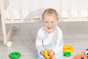 Portrait of a smiling child playing near the crib, baby boy 2 years old sitting with toys, early development