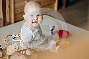 Portrait of a smiling child playing with toys while sitting on the floor in the nursery on the mat.