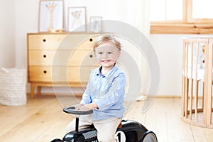 Portrait smiling  child riding toy vintage car. Funny kid playing at home. Summer vacation and travel concept. little boy driving