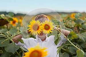 Portrait smiling child with sunflower in summer sunflower field on sunset. Kids happiness concept