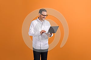 Portrait of smiling confident businessman doing online research over laptop on orange background