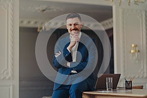Portrait of smiling confident businessman sitting on office desk