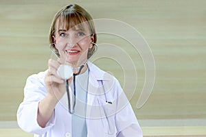 Portrait of smiling confident female doctor in white workwear holding stethoscope and standing in clinic hospital. Professional