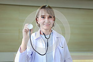 Portrait of smiling confident female doctor in white workwear holding stethoscope and standing in clinic hospital. Professional