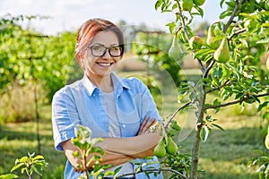 Portrait of smiling confident middle aged woman with crossed arms in orchard, near pear tree