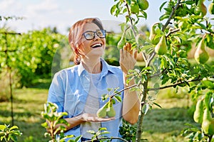 Portrait of smiling confident middle aged woman with crossed arms in orchard, near pear tree