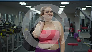 Portrait of smiling confident plus-size woman walking in gym looking around smiling. Front view of happy overweight