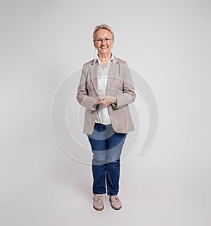 Portrait of smiling confident senior businesswoman with hands clasped standing on white background