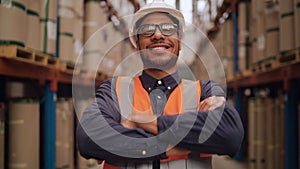 Portrait of a smiling confident warehouse worker in protecting hat standing with his arms crossed in a large warehouse