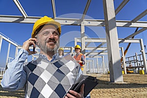 Portrait of Smiling Construction Foreman With Mobile Phone At Large Construction Site