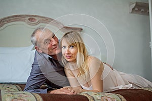 Portrait of Smiling Couple with Age Difference. Beautiful Young Woman with Her Senior Lover Lying on the Bed. Man