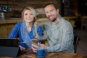 Portrait of smiling couple with coffee and technologies in cafe