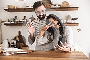 Portrait of smiling couple hugging together and holding smartphone while cooking in kitchen at home