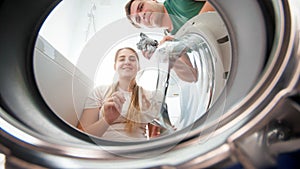 Portrait of smiling couple looking inside and washing machine in bathroom and loading i with dirty clothes. Family doing