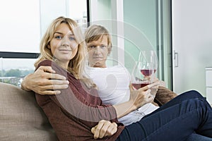 Portrait of smiling couple with wine glasses in living room at home