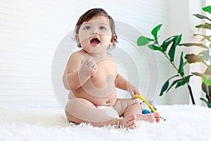 Portrait of smiling crawling baby sits on fluffy white rug, little cute kid girl playing with developmental toys, happy daughter