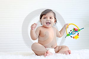 Portrait of smiling crawling baby sits on fluffy white rug, little cute kid girl playing with developmental toys, happy daughter