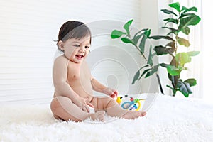 Portrait of smiling crawling baby sits on fluffy white rug, little cute kid girl playing with developmental toys, happy daughter