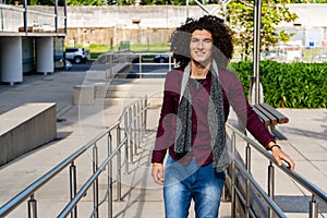 Portrait of a smiling curly haired young latino man wearing a shirt on the street. Copy space
