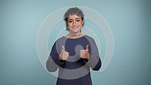 Portrait smiling curly woman raises hands shows like thumbs up looks camera