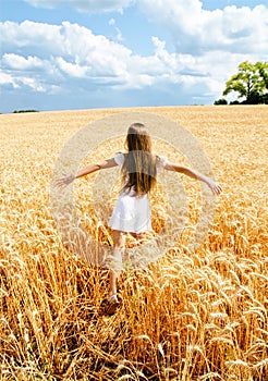 Portrait of smiling cute little girl child running through field of wheat