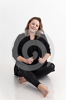 Portrait of smiling cute middle-aged fat plump woman with long dark hair and make-up sitting, holding black cardigan.