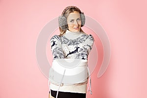 Portrait of smiling cute pretty woman 30-35 years in earmuffs, giving gift box with copy space, Studio shot on pink