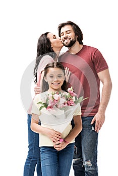 portrait of smiling daughter with bouquet of flowers with parents kissing behind photo