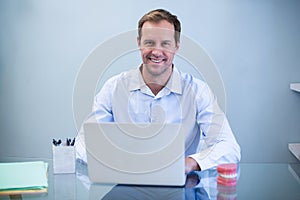 Portrait of smiling dentist working on laptop