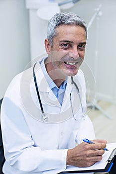 Portrait of smiling dentist writing on clipboard