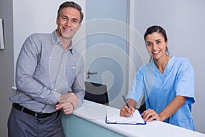 Portrait of smiling doctor holding pen standing by man at desk