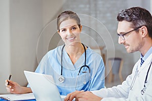 Portrait of smiling doctor sitting at desk with colleague