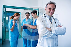 Portrait of smiling doctor standing with arms crossed in corridor