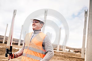 Portrait of smiling engineer on construction site, surveyor using gps system and theodolite on highway construction site