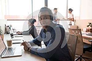 Portrait of smiling ethnic male agent in headset at workplace