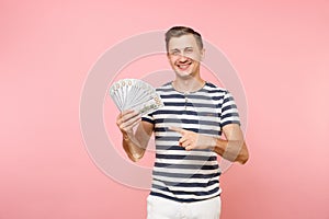 Portrait of smiling excited young man in striped t-shirt holding bundle lots of dollars, cash money, ardor gesture on