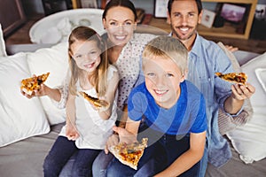 Portrait of smiling family holding pizza slices while sitting on sofa