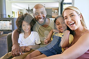 Portrait Of Smiling Family Hugging And Sitting On Sofa At Home Together