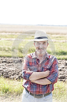 Portrait of smiling farmer standing with arms crossed on field at farm