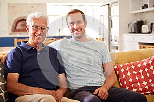 Portrait Of Smiling Father With Adult Son Relaxing On Sofa At Home