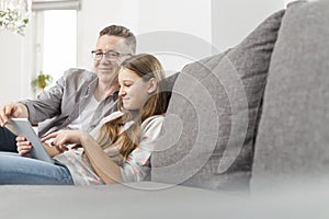 Portrait of smiling father assisting daughter in using digital tablet on sofa at home