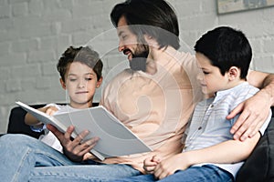 portrait of smiling father and sons reading book together