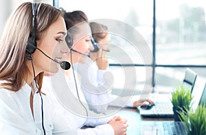 Portrait of smiling female customer service agent wearing headset with colleagues working in background at office.