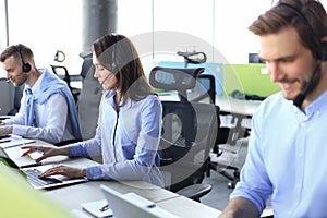 Portrait of smiling female customer service agent wearing headset with colleagues working in background at office