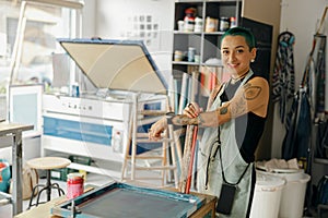 Portrait of smiling female designer standing on background of print machine in workshop